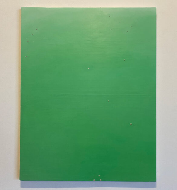 A photograph of a green rectangular painting hanging on a gallery wall. The painting has a handful of small white specks scattered across it. Artwork by Madi Ortega.