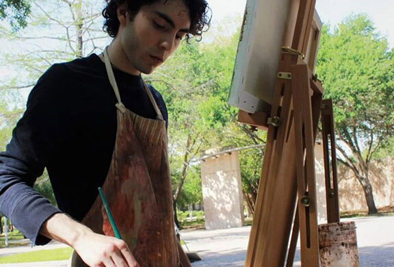 A photograph of Jesus Treviño standing at an easel and painting outdoors.