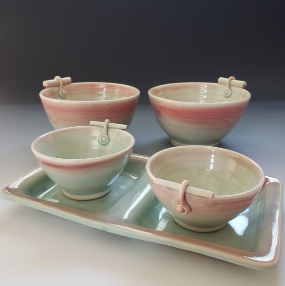 A photograph of a set of bowls painted with a gradient ranging from pink to green.